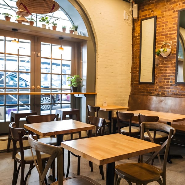 Interior of Plum Vietnamese Restaurant with wooden tables and chairs, brick walls, and large arched windows.
