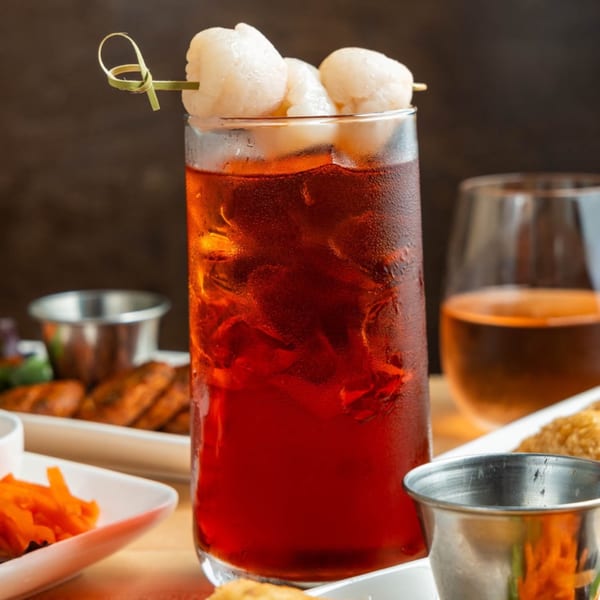 A tall glass of iced red Plum Vietnamese Restaurant drink, garnished with lychees on a skewer.