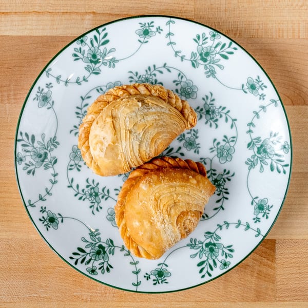 Two golden-brown Vietnamese curry puffs with crimped edges on a white plate with green floral patterns.