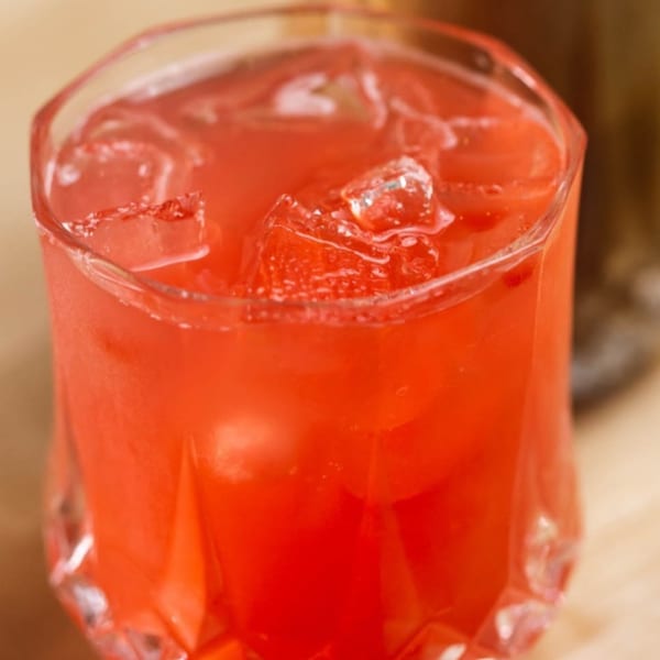 Close-up of a vibrant red drink with ice cubes in a faceted glass at Plum Vietnamese Restaurant.