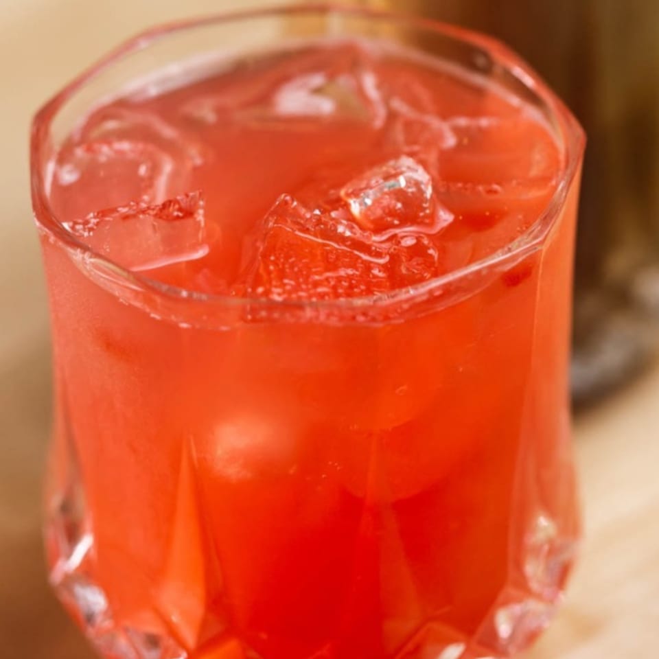 Close-up of a vibrant red drink with ice cubes in a faceted glass at Plum Vietnamese Restaurant.