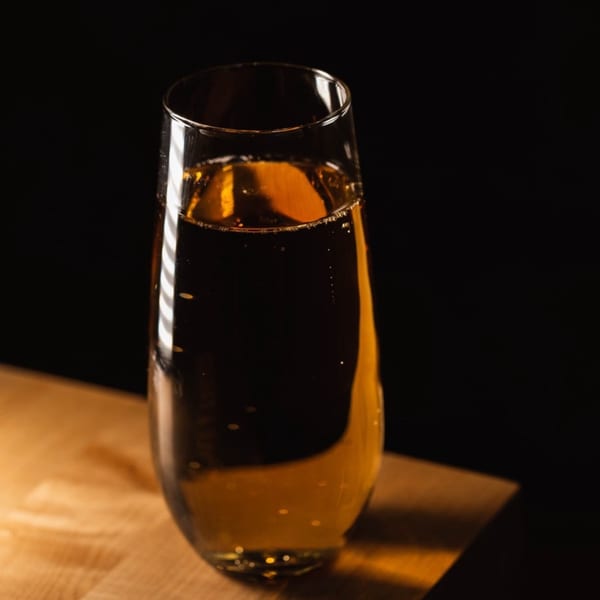 A tall, clear glass of sparkling golden liquid with bubbles, on a wooden surface.