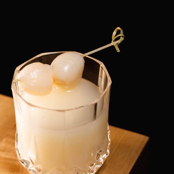 A Vietnamese lychee cocktail in a faceted glass, garnished with two lychees on a skewer.