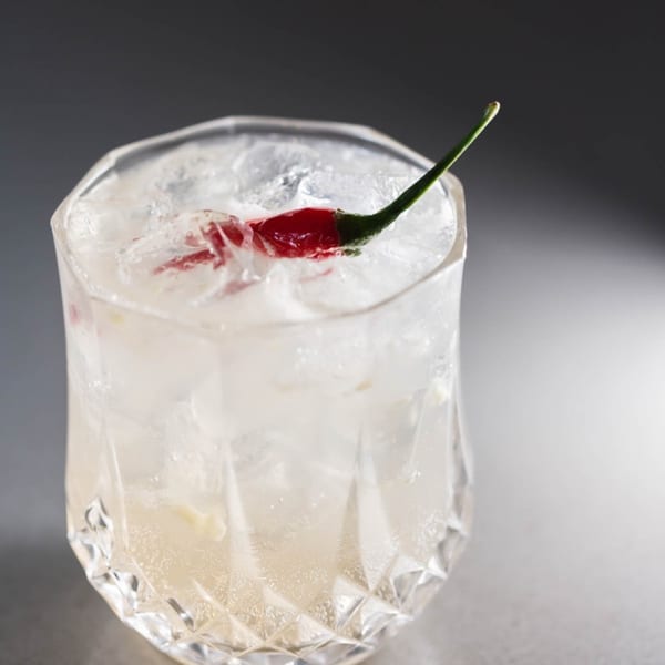 Iced Vietnamese cocktail in a faceted glass, garnished with a red chili pepper.