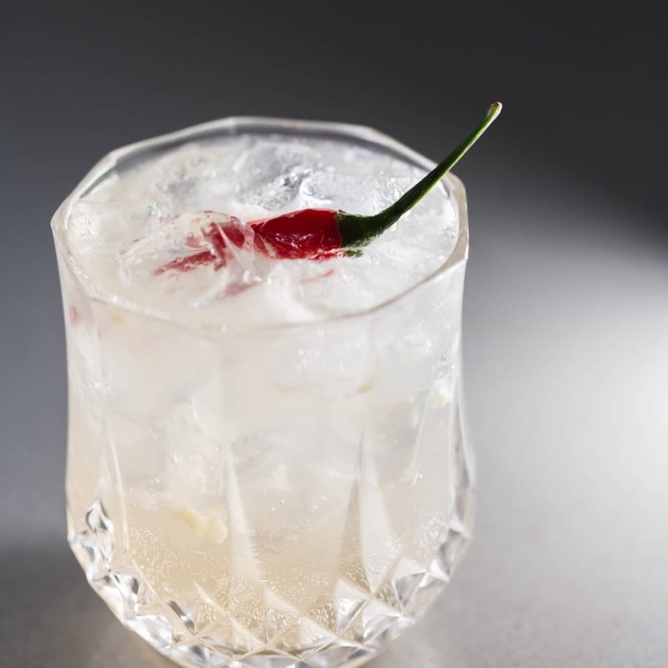 Iced Vietnamese cocktail in a faceted glass, garnished with a red chili pepper.