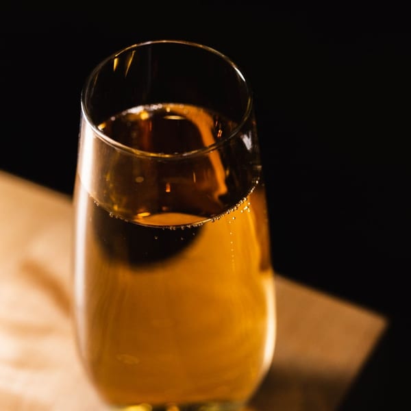 Close-up of a glass filled with a golden, bubbly beverage against a dark background.