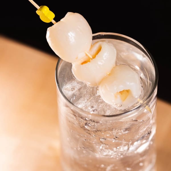 A clear glass of iced Plum Vietnamese Restaurant lychee drink, garnished with three lychees on a skewer.